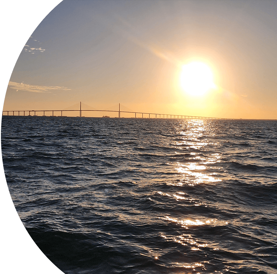 A sunset over the ocean with a bridge in the background.