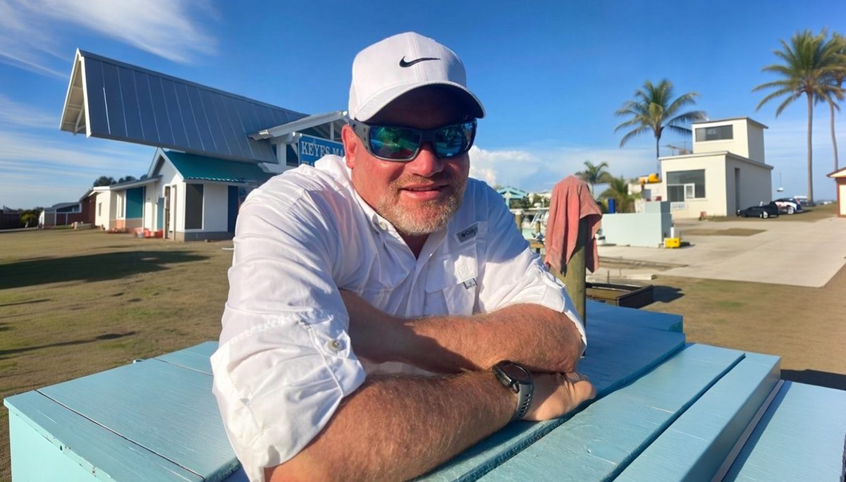 A man in white shirt and hat holding fish.