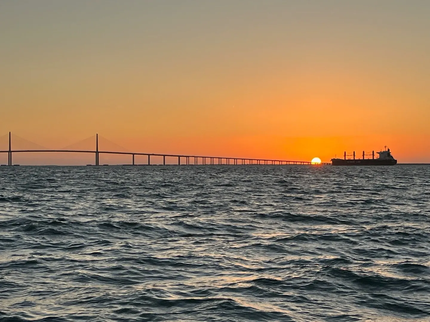 A sunset over the ocean with a bridge in the background.